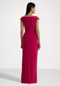 Fuksia off-the-shoulder mekko, jolla on istuva siluetti, lattiaan asti ulottuva leikkaus ja hienovarainen takareikä liikkumisen vuoksi, valmistettu sileästä, joustavasta kankaasta.