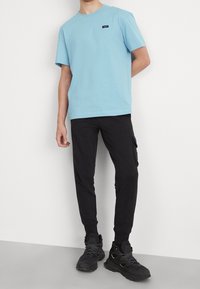 Ljusblå bomullströja med rund halsringning och liten logotyp; tillsammans med slim-fit svarta cargobyxor och svarta snörskor.