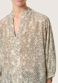 Blusa leggera e trasparente con un motivo astratto in verde tenue e beige, scollo a V e maniche 3/4 con polsini leggermente arricciati.