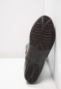 Chaussure en cuir noir avec semelle en caoutchouc texturée. Présente une finition lisse, un bout arrondi et une fermeture éclair sur le côté. Conçue pour le confort et le soutien.