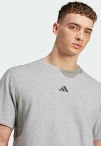 T-shirt gris à manches courtes en tissu mélangé coton avec un col rond et un logo Adidas noir sur la poitrine. Design doux et décontracté.