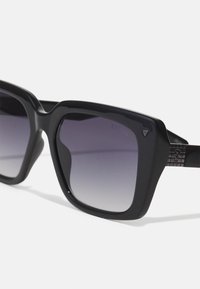 Ochelari de soare din plastic negru cu rame pătrate și lentile gri cu gradient. Prezintă accente metalice și detalii texturate pe brațe.