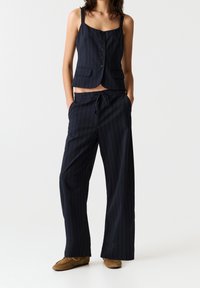 Veste courte à rayures bleu marine avec boutons et poches, associée à un pantalon ample bleu marine. Tissu doux, texture lisse, et taille à cordon de serrage.