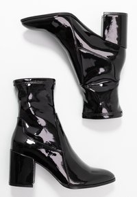 Botas de tobillo de charol negro con punta afilada, tacón grueso y un diseño sin costuras. Presentan costuras visibles y una textura suave.