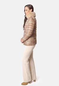 Chaqueta acolchada marrón con un patrón, cuello de pelo sintético beige en contraste, bolsillos laterales con cremallera y una silueta ajustada.