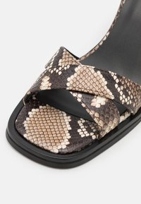 Sandale à bride croisée avec un motif serpent dans des tons de brun et de crème, avec une semelle noire et une semelle matelassée.