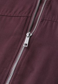 Silver metal zipper partially unzipped on a dark purple fabric background with visible stitching details.