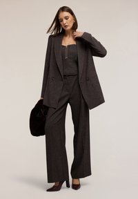 Dunkelgrau blazer mit taillierter Passform und doppelreihigen Knöpfen, passende weite Hose und ein enges Oberteil; accessoriert mit einer schwarzen Clutch und hohen Schuhen.