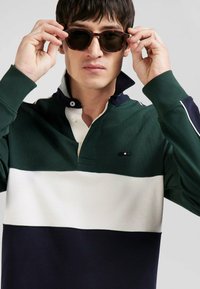 Polo à manches longues avec un design en blocs de couleurs, en vert foncé, blanc et marine. Caractéristiques d'un col et d'une patte de boutonnage.