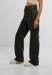 Schwarze hochtaillierte Jeans mit geradem Schnitt, ausgestattet mit Gürtelschlaufen, Fronttaschen und einem ausgefransten Saum; kombiniert mit weißen Sneakern.