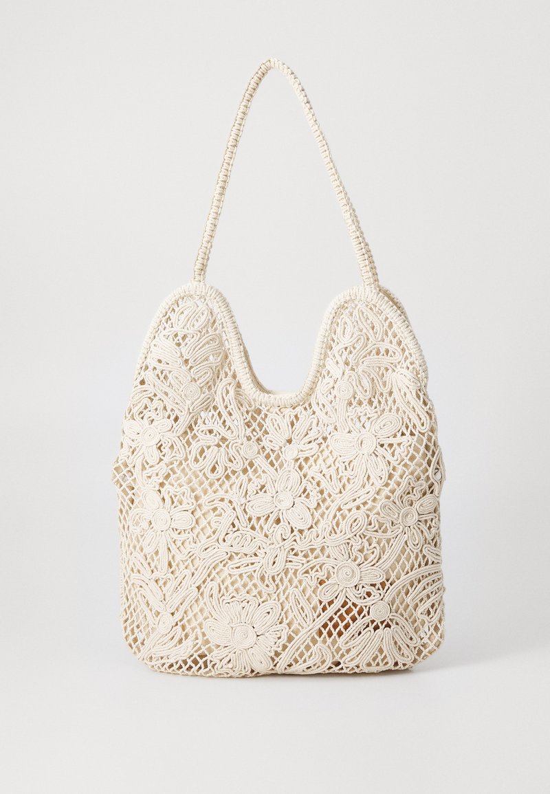 Beige crochet handbag with floral patterns, a rounded shape, and a woven handle. Features intricate lace-like detailing throughout.
