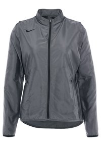 Šedá větrovka vyrobená z lehkého, hladkého materiálu. Má vysoký límec, plný zip a dvě boční kapsy. Černé logo Nike.