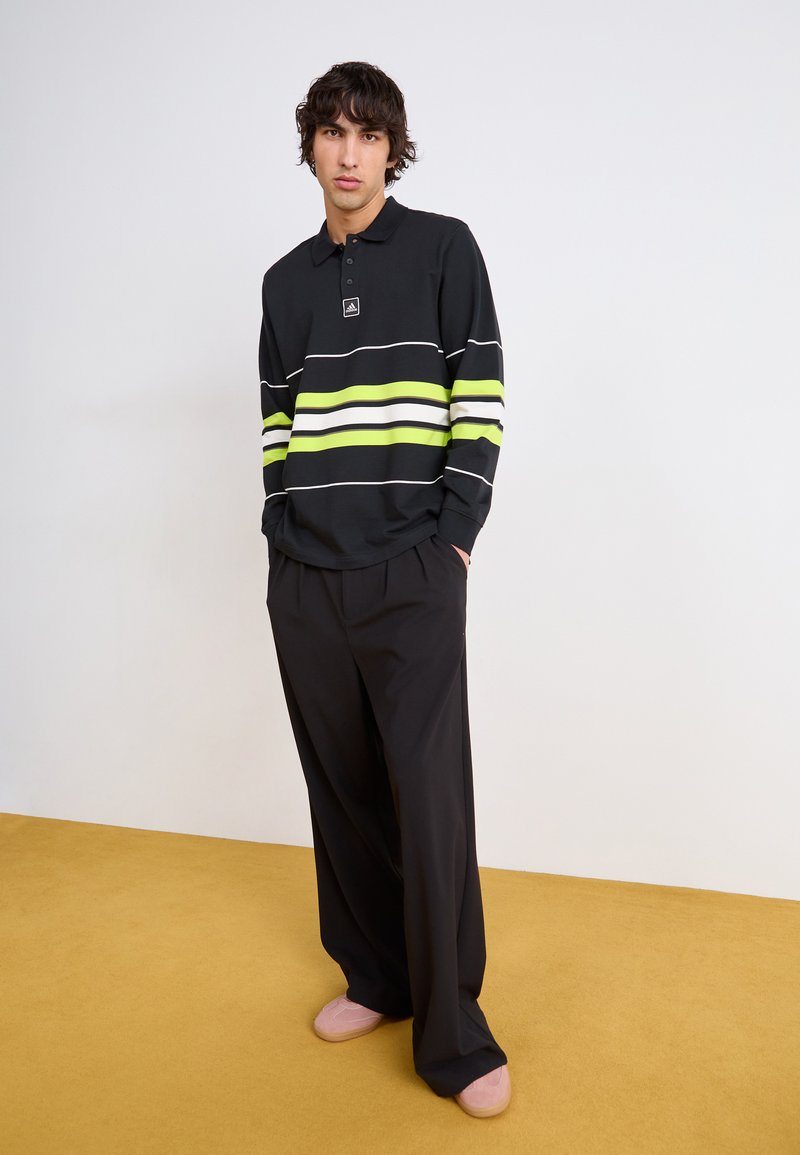 Polo noir à manches longues avec des rayures horizontales blanches et jaunes fluo. Matière douce, coupe décontractée, associé à un pantalon noir ample.