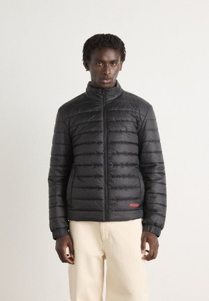 Black puffer jacket with horizontal stitching, high collar, and zip closure. Features ribbed cuffs and a red logo on the lower front.