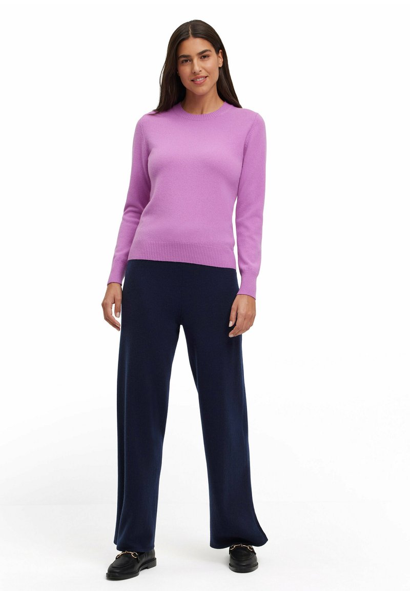 Lila Pullover in einem figurbetonten Design, gestrickte Textur, kombiniert mit dunkelblauen weit geschnittenen Hosen. Schwarze Schuhe runden das Outfit ab.