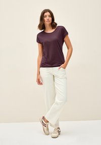 Lila kortärmad t-shirt med rund halsringning, i kombination med löst sittande vita byxor och beige sneakers med vinröda accenter.