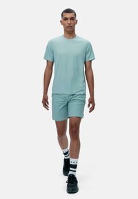 Svetlo modra majica s kratkimi rokavi in usklajene kratke hlače, narejene iz gladkega blaga. Model nosi črne superge in črtaste nogavice s črnimi poudarki.