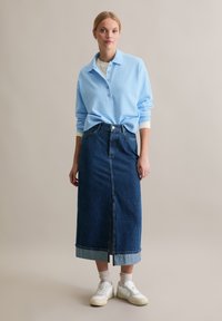 Jasnoniebieski sweter z kołnierzykiem i guzikami, w połączeniu z długą spódnicą dżinsową z przeszyciem z przodu i podwiniętym dołem, noszony z białymi trampkami.