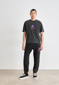 Grå, oversized t-skjorte med kort erme og rosa grafikk, parret med matchende grå joggebukser med logo. Svarte sneakers med hvite såler.