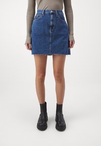 Jeans mini kjol i mörkblått med fransad fåll, med bältesöglor och sidofickor, parat med svarta ankelboots.