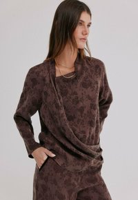 Haut à manches longues à motif floral marron avec un col drapé, une texture douce et deux poches latérales. Stylé avec des colliers en or superposés.