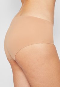 Beige puuvillasekoitemateriaalist istuvad aluspüksid, millel on sile tekstuur, keskmise kõrgusega disain ja õmblusteta konstruktsioon mugavuse tagamiseks.
