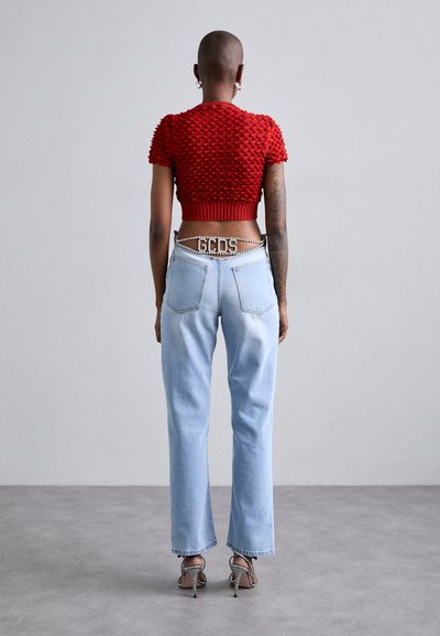 Top corto de textura roja con mangas abullonadas, combinado con jeans rectos de color azul claro y un cinturón con acentos de cristal. Sandalias de tacón destalonadas.