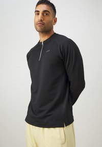 Fekete hosszú ujjú sportpóló félcipzárral a nyaknál, textúrált oldalpanelekkel és slim fit szabással. Sima anyag és minimális márkajelzés.