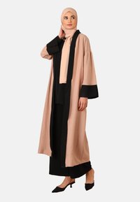 Lang, flydende kimono-lignende beklædning i beige og sort, med brede ærmer og en kontrasterende sort kant langs fronten og ærmerne.