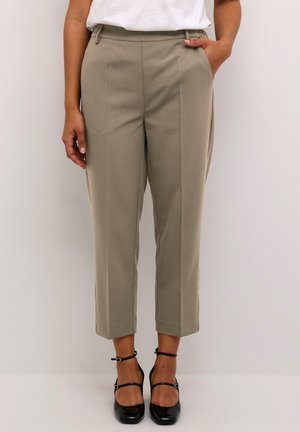 Beige tailored trousers with a high waist, pleated details, and side pockets. Paired with black strap heels. Smooth texture, cropped length.