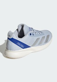 Ljusgrå sportskor med blå "Pickleball"-text, silverstrimmor, nätovandel och vit sula, visad från bakre sidovinkel.