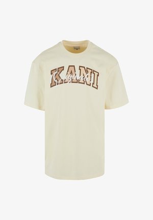 Kremna majica s okruglim izrezom, kratkim rukavima i podebljanim smešnim natpisom "KANI" u smešnoj braon boji, dok je ispod napisan "Originato" u beloj kurzivnoj fontu.