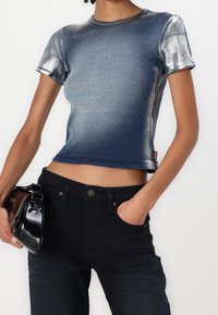 Metallisk blå kortärmad t-shirt med ribbad textur, rund halsringning och synlig sömnad; tillsammans med högmidjade mörk denimjeans.