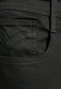 Schwarze Denim-Jeans verfügen über eine kleine Gesäßtasche mit kontrastierendem Stich. Der Stoff hat eine glatte Textur und einen subtilen Glanz.