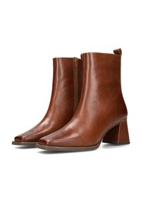 Botas de tobillo de cuero marrón con cremallera lateral, tacones de bloque y punteras puntiagudas sobre un fondo blanco.