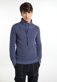 Dunkelblauer Strickpullover mit hohem Kragen und Kordelzug, aus strukturiertem Stoff mit enganliegenden Ärmeln, kombiniert mit schwarzen Cargo-Hosen.