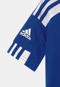 Modrá sportovní dres s bílými akcenty. Obsahuje tři bílé pruhy na rameni a vyšitou logo Adidas na rukávu.