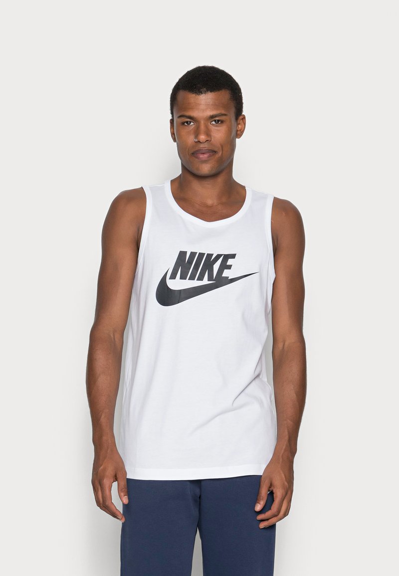 Bela bombažna majica brez rokavov z besedilom črnega Nike logotipa na sredini prsnega dela. Ima okroglo ovratnico in brezrokavni dizajn.