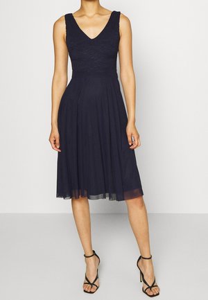Vestido sin mangas azul marino hasta la rodilla con escote en V y cuerpo ajustado, combinado con sandalias negras de tacón alto con tiras.