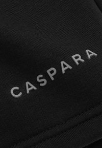 Svart stoff med en teksturert overflate som har ordet "CASPARA" i subtil grå farge, sentrert og med små bokstaver, nær bunnen av kanten.