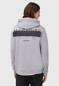 Lichtgrijze hoodie met een groot zwart "ALLSAINTS" logo op de rug, met aanvullende tekst in het Japans en "LONDEN" eronder.