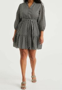 Vestido de estampado en blanco y negro con escote en forma de V, mangas abullonadas, cinturilla y falda con volantes en capas. Combinado con tacones de tiras en tonos neutros.