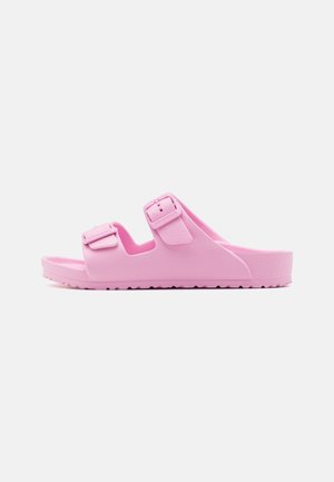 Roze slip-on sandaal met twee verstelbare gespen en een getextureerde zool, zijaanzicht op een witte achtergrond.