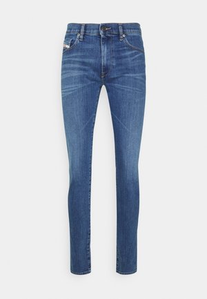 Vaqueros slim fit azul medio con cierre de botón y cremallera, bolsillos en la parte delantera y trasera, y detalles de desgaste sutil en los muslos.