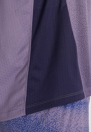 Gros plan sur un panneau de tissu avec des sections verticales aux nuances de violet et des motifs texturés sur un matériau de vêtements de sport.