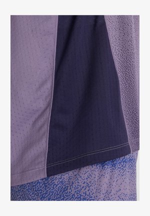Gros plan sur un panneau de tissu avec des sections verticales aux nuances de violet et des motifs texturés sur un matériau de vêtements de sport.