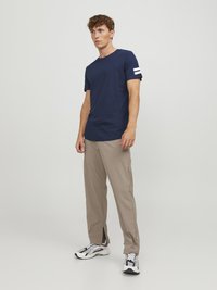 Marineblå crew neck t-shirt med hvide striber på venstre ærme, parret med lyse beige bukser og sort-hvide sportsko.