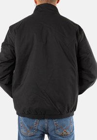 Giacca bomber nera con colletto alto, vita elasticizzata e maniche arricciate. Realizzata in tessuto liscio e resistente, senza loghi visibili.