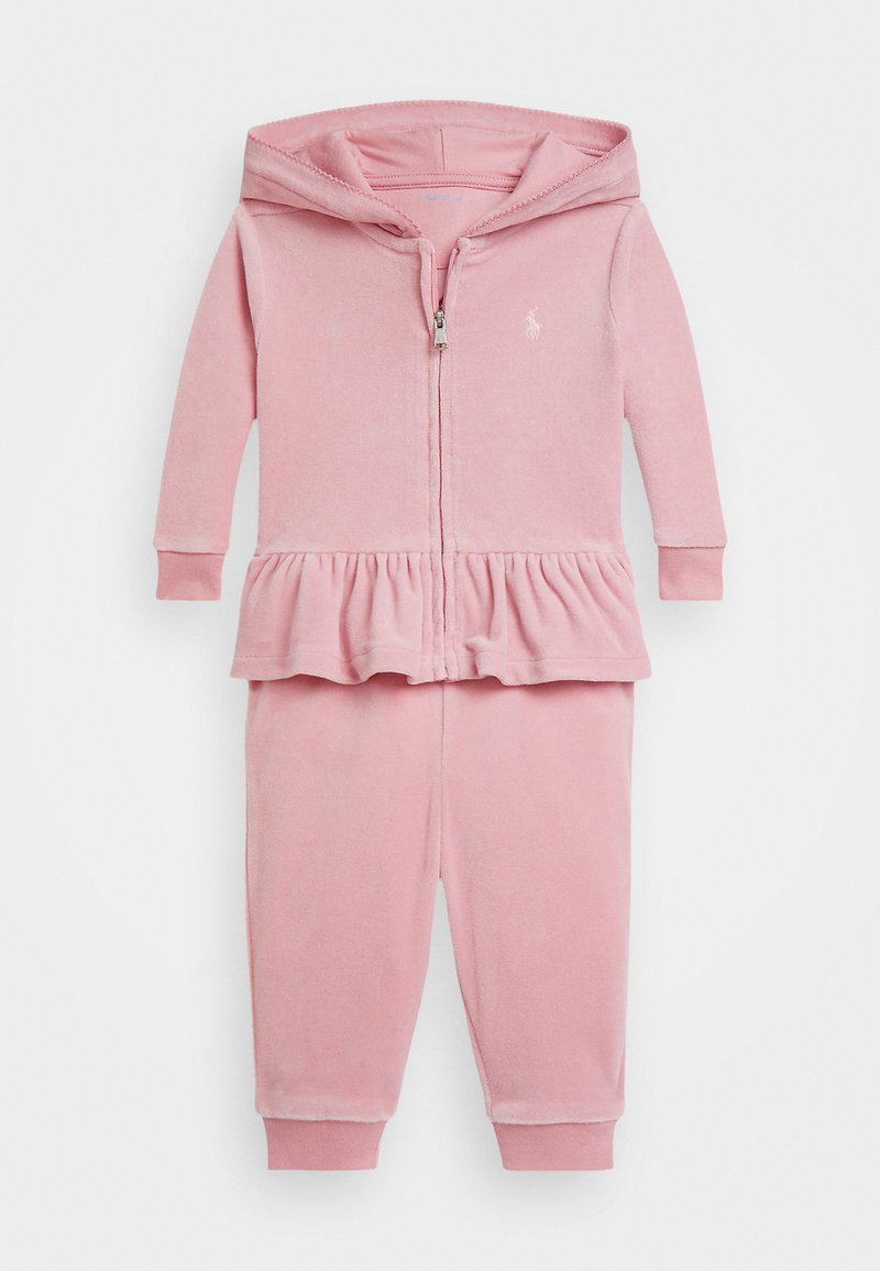Ružový sametový teplákový komplet s mikinou na zips a kapucňou, ktorá má peplum spodný lem, a zodpovedajúcimi nohavicami so sťahovaním na členkoch.