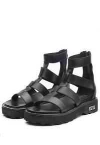 Sandali in pelle nera con più fascette orizzontali, punta aperta, altezza alla caviglia e suola in gomma testurizzata. Presentano una cerniera per una facile vestibilità.